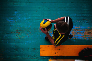 Man with volleyball in gymnasium, top view on blue wooden background. Position of hands and ball in the form of a heart, day of volleyball players in love. Team volleyball game © Oxana