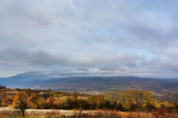 Beautiful autumn landscape with a view of the mountain in nature with yellow and golden colored forest and meadow on a cold cloudy day
