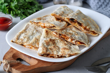 Mexican snack quesadilla from tortilla with chicken, cheese and mushroom in white plate on wooden board