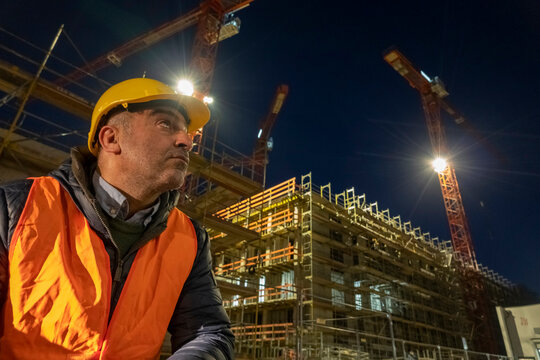 Construction worker sitting outdoors at night wearing a safety vest and a protective hardhat