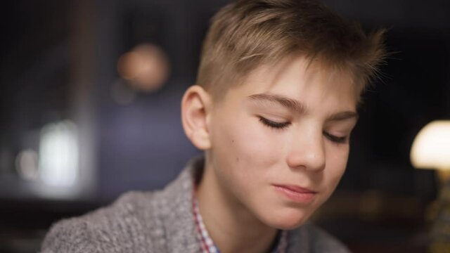 Headshot portrait smiling handsome teenage Caucasian boy dining in restaurant with parents eating delicious sausage in slow motion. Close-up happy teenager enjoying dinner indoors