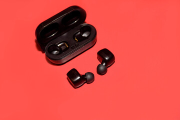 Black wireless bluetooth headphones or earbuds isolated on a scarlet background.