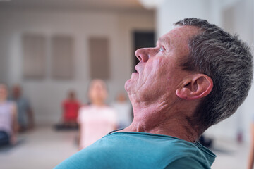 Obraz premium In the foreground an older adult man, yoga instructor, stretching his back. In the background his students imitating the pose.