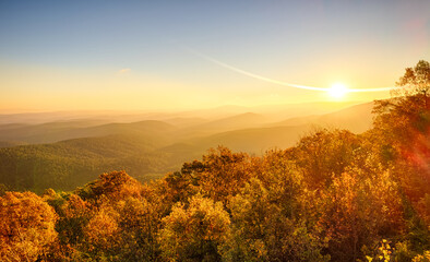 Sunrise in November over scenic mountaintop in Ouachita National Forest, with fall colors, heavy mist and fog in valleys, and sun flares - obrazy, fototapety, plakaty