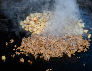 Sausage cooking on a griddle, and hash brown on the background; with heavy steam rising from the...