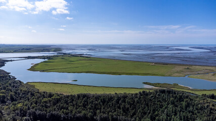 Luftaufnahme des Katinger Watt, Wald sowie einen idyllischen See im Vordergrund und im Hintergrund die Nordsee und das Wattenmeer bei blauem Himmel und Sonne