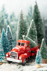Christmas scene with a red truck between evergreen trees in snow