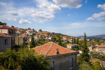 Fototapeta na wymiar Panorama of the small town with bright red roofs on the hill with mountains on horizon white clouds on the blue sky