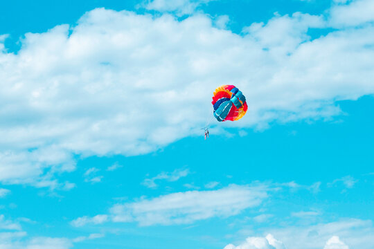 Parasailing couple with colourful rainbow parachute in front of blue sky and clouds