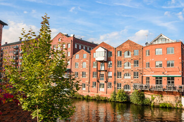 Old brick warehouses converted into lofts along a river on a sunny autumn day. Leeds, UK.