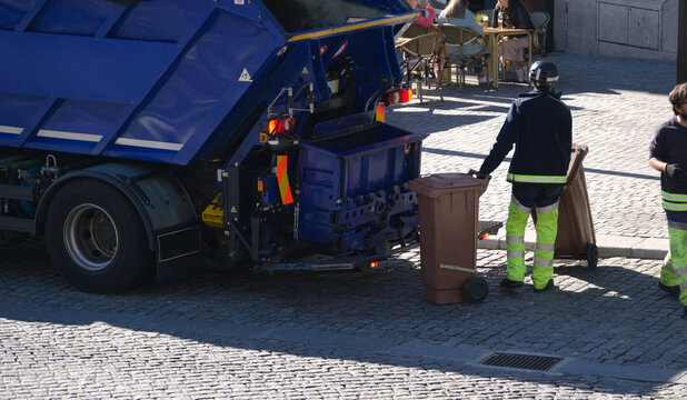 Camião de recolha de lixo com um homem a colocar contentores de lixo para serem despejados dentro do camião - limpar a cidade