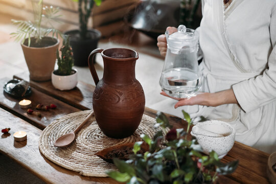 Pouring water into jug with cacao. Preparing ceremonial cocoa in atmospheric boho style cafe full of plants. Woman cooking healthy drink from organic cacao beans for ritual 