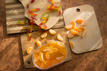 Orange jelly in a plastic container with tangerine slices on wooden planks.