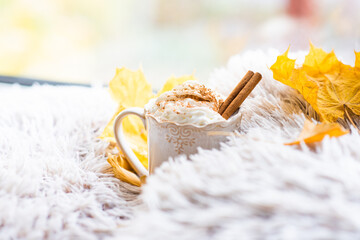 Obraz na płótnie Canvas Fall sweet coffee on a soft blanket on the windowsill, cozy autumn morning concept, delicious coffee with whipped cream and cinnamon stick