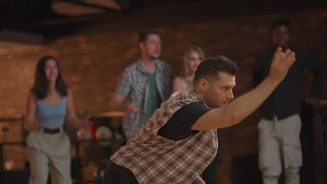 Portrait A young Caucasian man makes the final throw with a bowling ball and wins the game with the support and joy of his friends of different nationalities. Rejoice and celebrate the victory