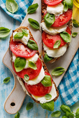 Caprese open faced sandwich based on sourdough bread with the addition of tomatoes, mozzarella cheese, fresh basil and olive oil on a white board top view