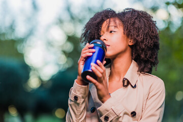 Obraz premium Drinking coffee drink outdoors in winter from a thermos. Latinx woman with afro curly hair