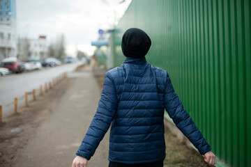 The guy walks along the fence. A man in a black hat.