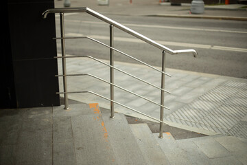 Shiny gray curved metal railings on the stairs, exit from the store. Urban infrastructure. The street of the metropolis in scattered daylight