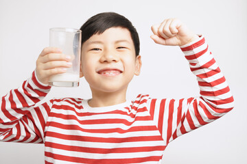 Happy and strong asian little boy hold a glass of milk and lift up his arms to show how healthy he...