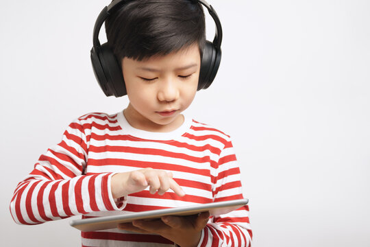 Portrait of an adorable smart asian student boy with headphone using tablet computer to join online classroom learning from home during Covid-19 pandemic. Internet technology, Digital, Touch screen