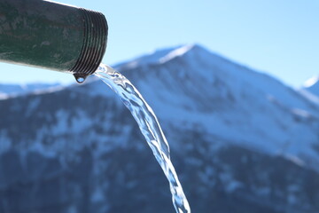 Naklejka na ściany i meble fresh clean water comes out of the mountain tap close up, soft blurred mountain on the background