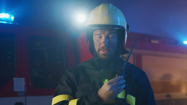 Mid adult firefighter man talking to walkie talkie with fire truck in background at night.