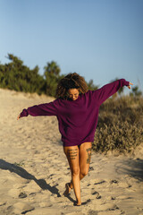 Vertical shot of a sexy tattooed female in a long purple sweater posing on a beach