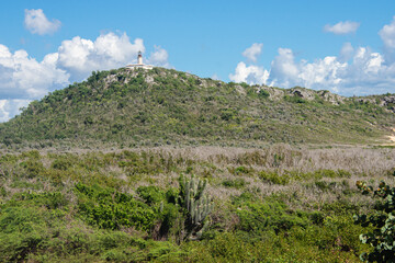 Fototapeta na wymiar The Caja de Muertos Lighthouse can be seen on the top of a hill covered with dry forest on the Island of Caja de Muertos off of the coast of Ponce in Puerto Rico, USA.