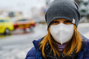 Front view close up portrait of adult caucasian woman standing outdoor in winter day wearing jacket and protective face mask to prevent covid-19 coronavirus spread in pandemic - real people copy space