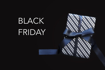 Black Friday sale, Gift box wrapped in black striped paper and tied with black bow on black background. 