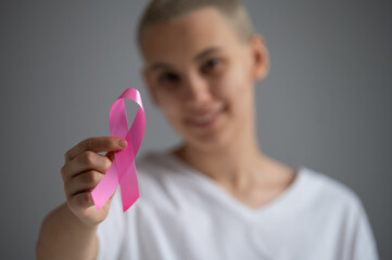 A faceless woman wearing a white t-shirt holds a pink ribbon as a symbol of breast cancer on a...