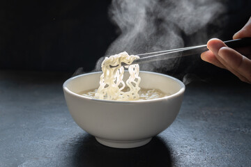 Lift with wood chopsticks  to pickup noodle with steam and smoke  on black background. korea, japan, china, Vietnam and Asian noodle junk food concept
