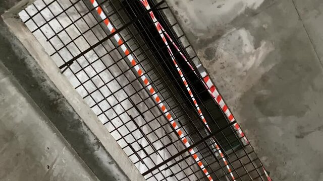 A large rectangular opening in the concrete floor is covered with an iron grating and shielded with protective tape