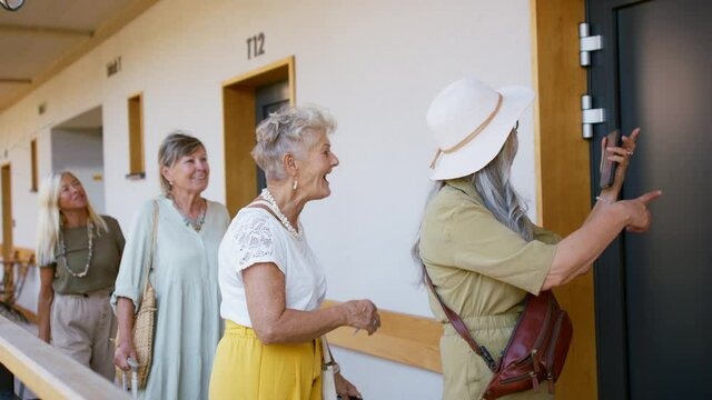 Senior women friends with suitcases standing in front of hotel room outdoors on terrace.
