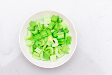 Fresh Chopped Celery Slices with Water Drops on White Dish - Top View. Vegan and Vegetarian Culture. Raw Food. Healthy Diet with Negative Calorie Content