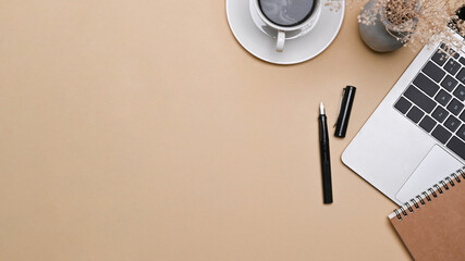 Top view laptop computer, cup of coffee and notebook on beige background.