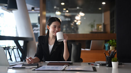 Smiling asian businesswoman drinking coffee and working in modern office.