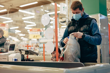 Obraz na płótnie Canvas Man in protective medical mask buying food at grocery store or supermarket during quarantine, lockdown, coronavirus pandemic.