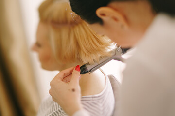 Hairdresser makes the girl styling with a curling iron. Close-up. Side view