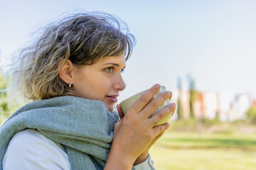 Woman in scarf drinking with a cup outdoors