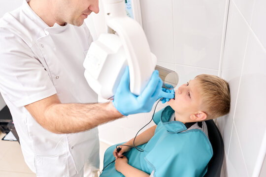 Radiographer taking teeth radiography to a boy using digital x-ray machine in pediatric dental clinic. Dentist prepares boy for tooth x-ray image in dental clinic.
