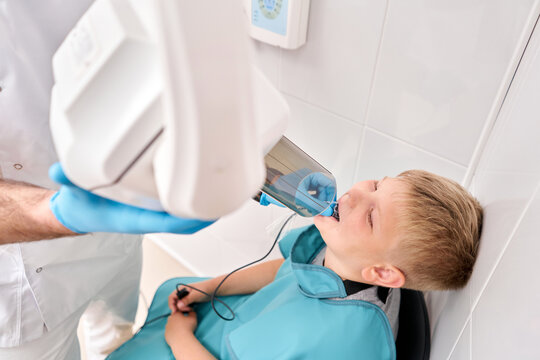 Radiographer taking teeth radiography to a boy using digital x-ray machine in pediatric dental clinic. Dentist prepares boy for tooth x-ray image in dental clinic.