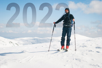 Fototapeta na wymiar A happy young man who reached the new year 2022 summit. Backcountry skiing in the mountains.
