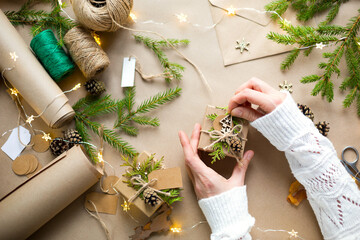 Hands in a white sweater pack a gift for Christmas and new year in eco-friendly materials: kraft...