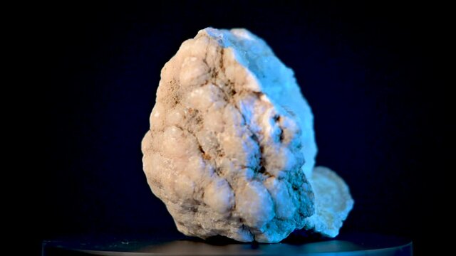 Large quartz crystal in rock on a rotating display stand.  Black background and blue accent lights show off sparkling crystals in up close view.
