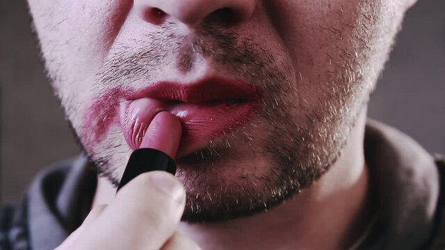 Close up of a young bearded man puts red lipstick on his lips. Man getting makeup. Lgbt concept