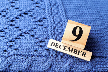 December 9th, 
Wooden calendar showing date on 9 December on blue knitted sweater.