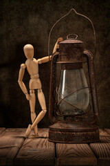 A wooden man and an old rusty kerosene lamp on a wooden table and an artistic background.