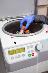 A hand in a blue glove puts a test tube into the centrifuge. Analysis of the quality of products.